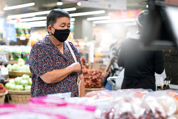 Oude senior aziatische vrouw draagt een virusverspreidingsbeschermingsmasker tijdens het winkelen met verse groenten en fruit in de supermarkt in de supermarkt nieuwe normale levensstijl nadat de lockdown voorbij is