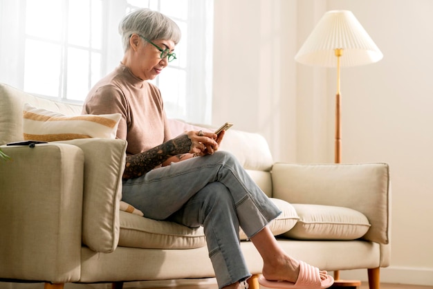 Oude senior aziatische vrouw met tatoeage zit casual ontspannen hand gebruik smartphone technologie apparaat video-oproep om begroeting en gesprek te hebben met haar familie witte thuisisolatie quarantaine periode moment