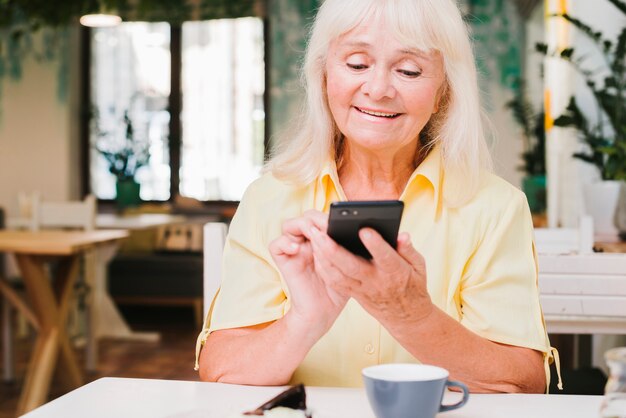 Oude vrouw die smartphone thuis gebruikt