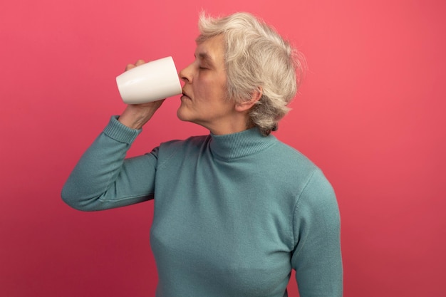 Oude vrouw met blauwe coltrui die kopje thee drinkt met gesloten ogen