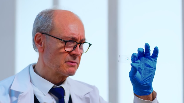 Oude wetenschapper man analyseert virusmonster in uitgerust laboratorium. Wetenschapper die werkt met verschillende bacteriën, weefsel- en bloedmonsters, farmaceutisch onderzoek naar antibiotica tegen de pandemie van het coronavirus