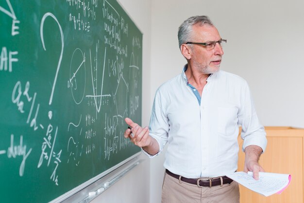 Oude wiskundeleraar die formule verklaart bij klaslokaal