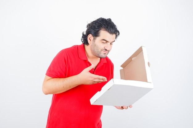 Ouder mannetje dat geopende pizzadoos in rood t-shirt bekijkt en verrukt kijkt. vooraanzicht.