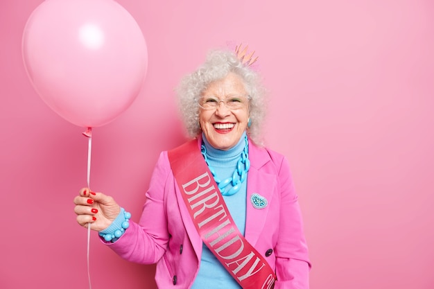 Gratis foto oudere gekrulde senior gerimpelde vrouw met opgeblazen ballon viert verjaardag