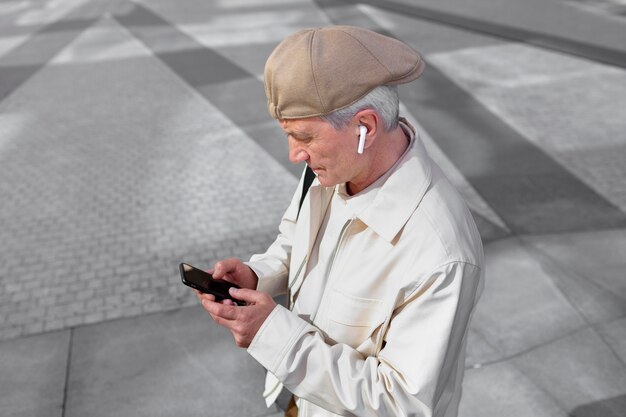 Oudere man buiten in de stad met smartphone met oordopjes