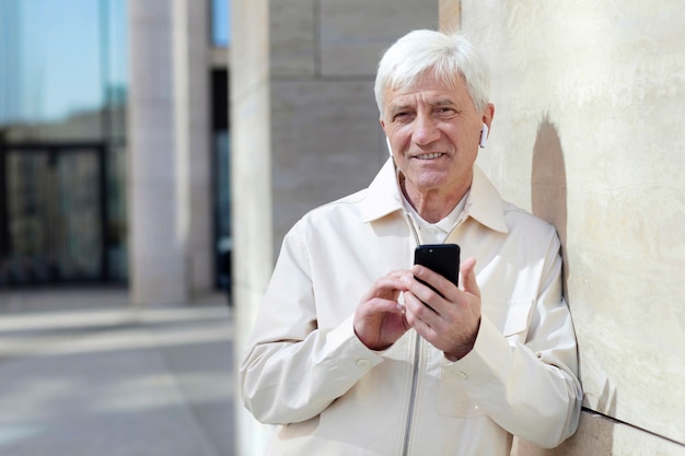 Oudere man buiten in de stad met smartphone met oordopjes