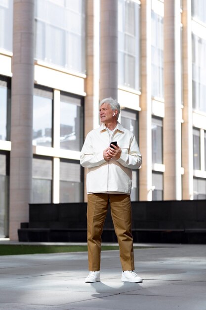 Oudere man buiten in de stad met smartphone met oordopjes