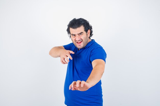 Oudere man die zich rechtop bevindt terwijl hij in blauw t-shirt, spijkerbroek staat en boos kijkt. vooraanzicht.