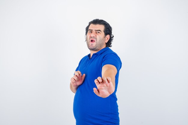 Oudere man die zich rechtop bevindt terwijl hij in blauw t-shirt, spijkerbroek staat en boos kijkt. vooraanzicht.