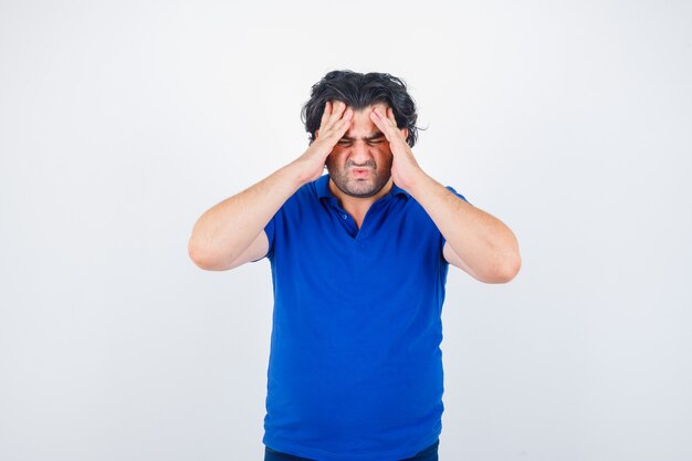 Oudere man in blauw t-shirt hoofdpijn lijden en op zoek geërgerd, vooraanzicht.