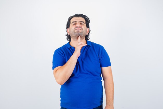 Oudere man in blauw t-shirt met zelfmoordgebaar en peinzend, vooraanzicht op zoek.