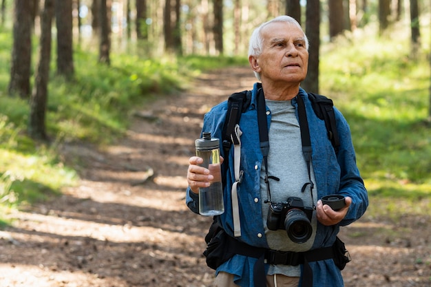 Gratis foto oudere man in de natuur met camera en waterfles