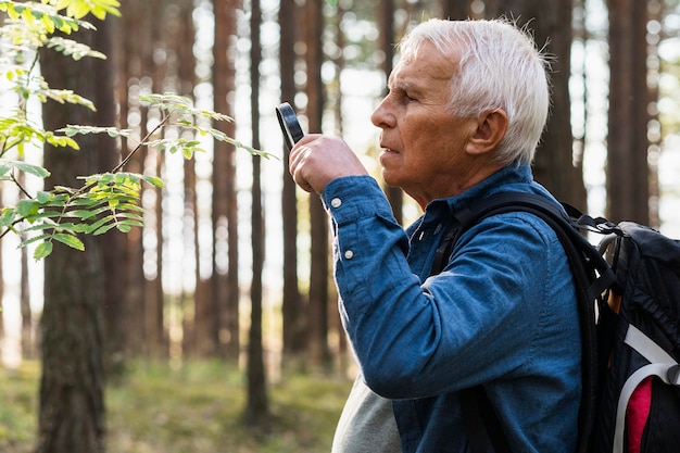 Oudere man met vergrootglas tijdens het verkennen van de natuur met rugzak