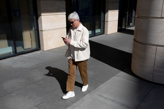 Oudere man met zonnebril buiten in de stad die smartphone gebruikt terwijl hij koffie drinkt