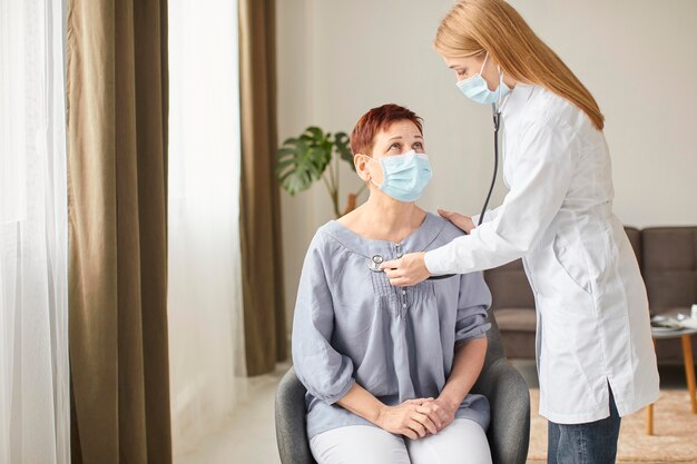 Oudere patiënt met medisch masker wordt gecontroleerd door de vrouwelijke arts van het covid-herstelcentrum
