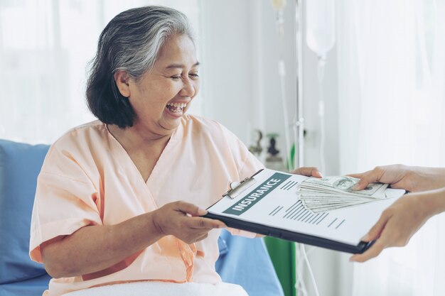 Oudere patiënten verwond vrouw op het bed van de patiënt in het ziekenhuis met ons dollarbiljetten voelen zich gelukkig van het krijgen van verzekeringsgeld van verzekeringsmaatschappijen