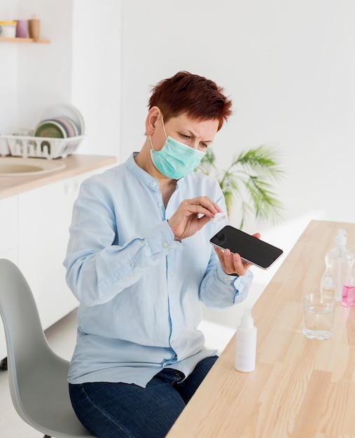 Oudere vrouw die haar smartphone reinigt terwijl het dragen van medisch masker