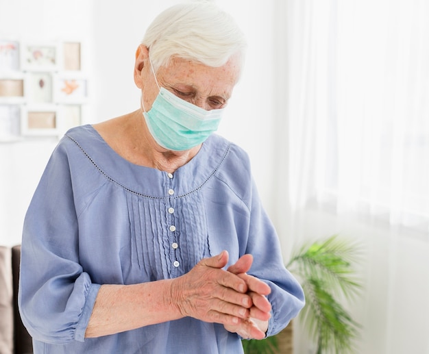 Oudere vrouw die met medisch masker thuis bidt