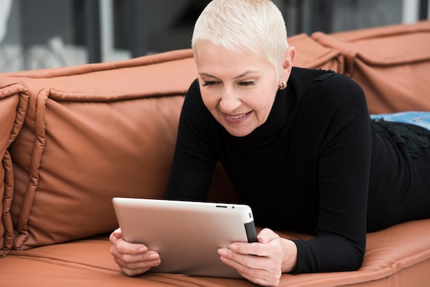 Gratis foto oudere vrouw die terwijl het bekijken tablet op bank glimlacht