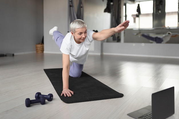 Oudere vrouw die yoga doet op een yogamat in de sportschool