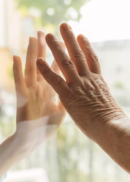 Oudere vrouw hand aanraken met iemand door raam tijdens de pandemie