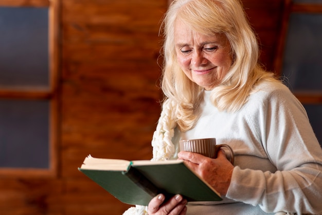 Gratis foto oudere vrouw het drinken van thee en lezen