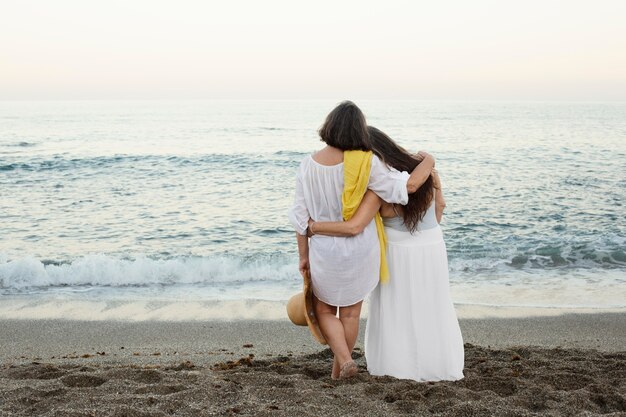 Oudere vrouwen die samen de oceaan bewonderen terwijl ze omarmd worden op het strand