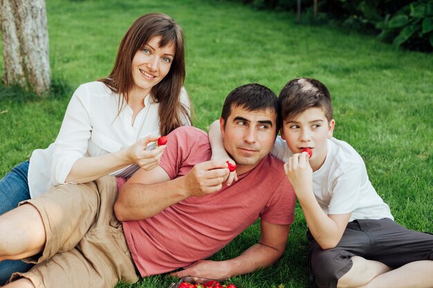 Ouders met hun zoon zittend op het gras en het eten van aardbeien
