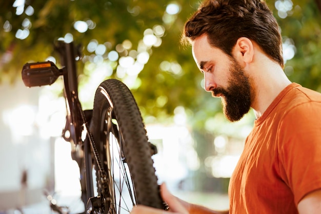 Outdoor close-up van een jonge blanke man die het rubber op zijn fietsband bevestigt en verandert voor jaarlijks onderhoud een vastberaden mannelijke fietser onderzoekt een beschadigd fietswiel in zijn achtertuin