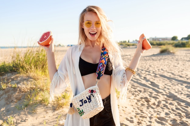 Outdoor lifestyle portret van speelse zorgeloze vrouw poseren met smakelijke grapefruit helften in handen.