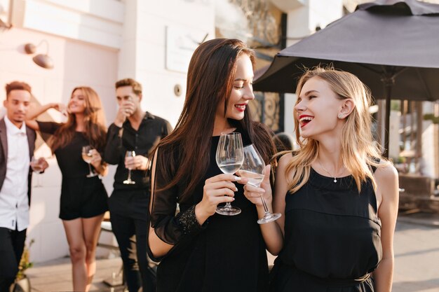 Outdoor portret van enthousiaste brunette vrouwen in zwarte jurken poseren