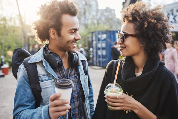 Outdoor Portret van twee schattige Afro-Amerikaanse mensen opknoping rond park, koffie drinken, lachen en praten.