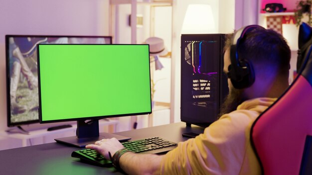 Over schouder beelden van man spelen van videogames op computer met groen scherm. Professionele gamer.