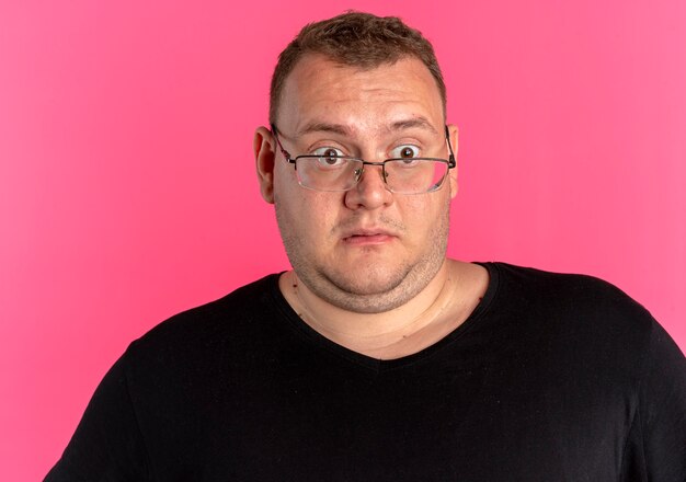 Overgewicht man in bril met zwart t-shirt opzij kijken verbaasd en verbaasd staande over roze muur