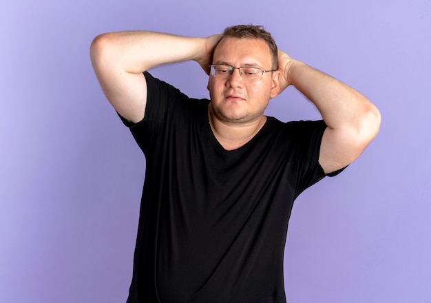 Overgewicht man in glazen met zwart t-shirt opzij kijken blij en positief staande over blauwe muur