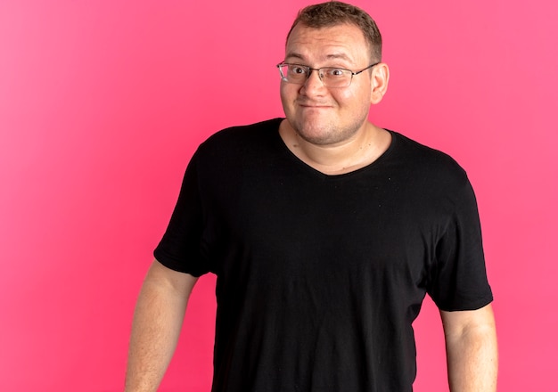 Gratis foto overgewicht man in glazen met zwarte t-shirt verward lachend over roze