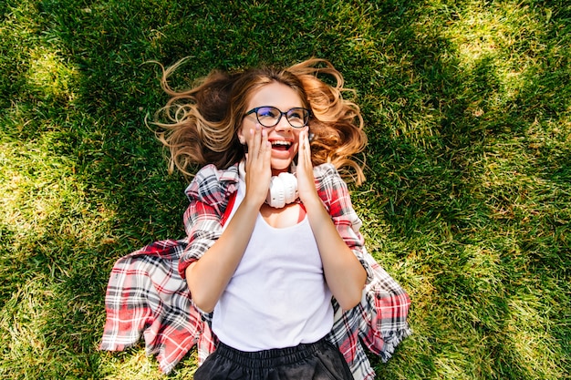 Gratis foto overhead portret van blij kaukasisch meisje dat op gras ligt. ontspannen schattige dame chillen in zomerdag.