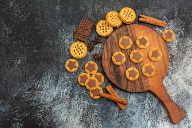 Overhead shot van koekjes op houten schotel met kaneel en koekjes en chocolaatjes op grijze grond