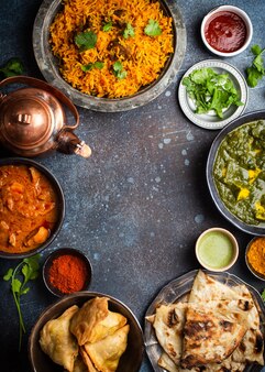 Overhead van indiase traditionele gerechten en hapjes: kip curry, pilaf, naan brood, samosa's, paneer, chutney op rustieke achtergrond. tafel met keuze aan gerechten uit de indiase keuken, ruimte voor tekst
