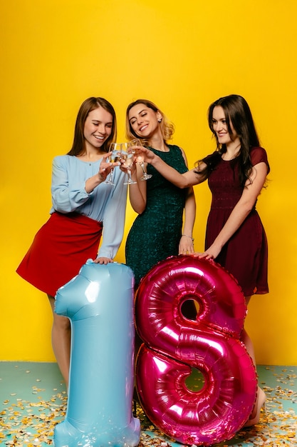 Gratis foto overweldigende jonge vrouwen die met champagne roosteren, die ballon in vorm van achttien houden