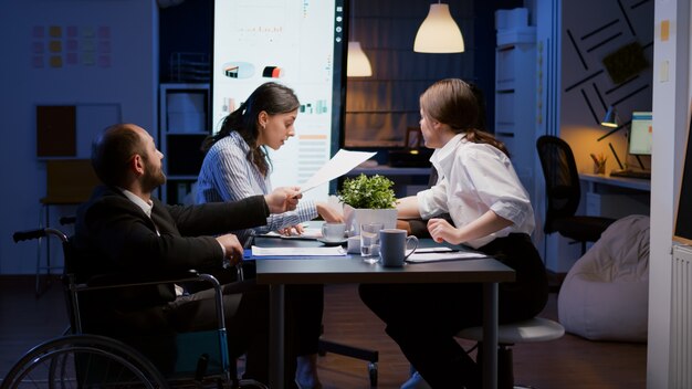 Overwerkte verlamde gehandicapte ondernemer man in rolstoel zit aan bureau overwerk in bedrijf...