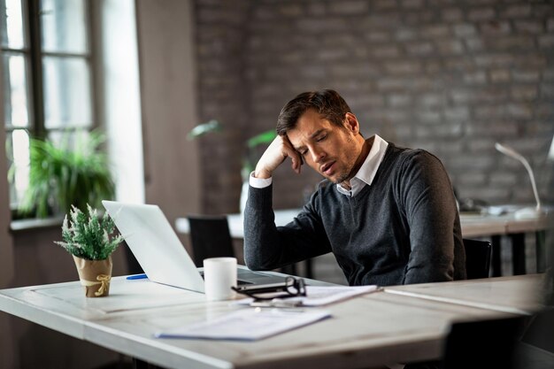 Overwerkte zakenman die aan zijn bureau zit en aan iets op kantoor denkt