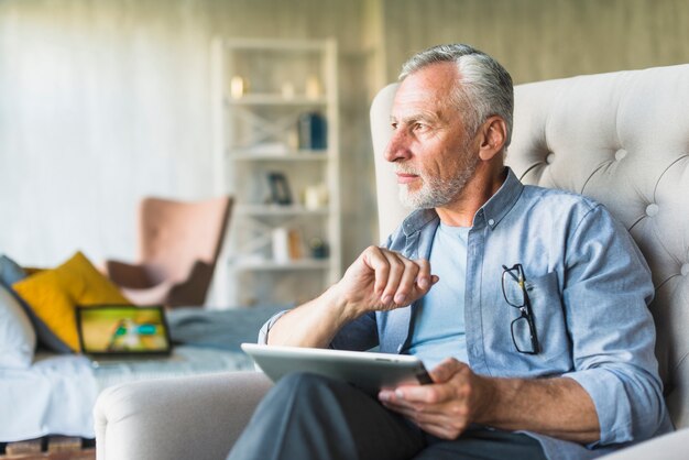 Overwogen hogere mens die digitale tablet houdt weg kijkend