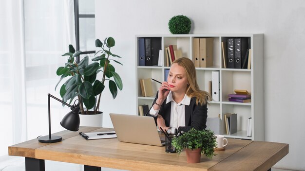 Overwogen jonge onderneemster die laptop in het bureau bekijkt