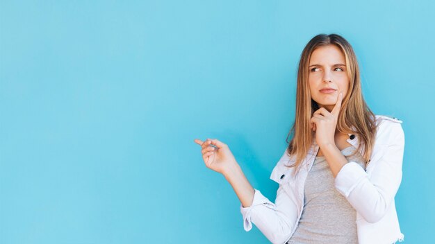 Overwogen jonge vrouw wijzende vinger tegen de blauwe achtergrond