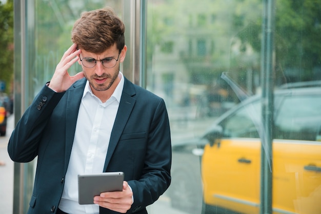 Gratis foto overwogen jonge zakenman die digitale tablet bekijkt