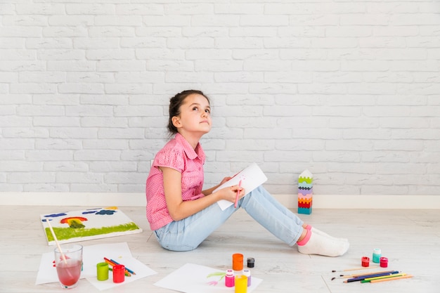 Overwogen meisjeszitting die op vloer op Witboek met kleurpotlood trekken