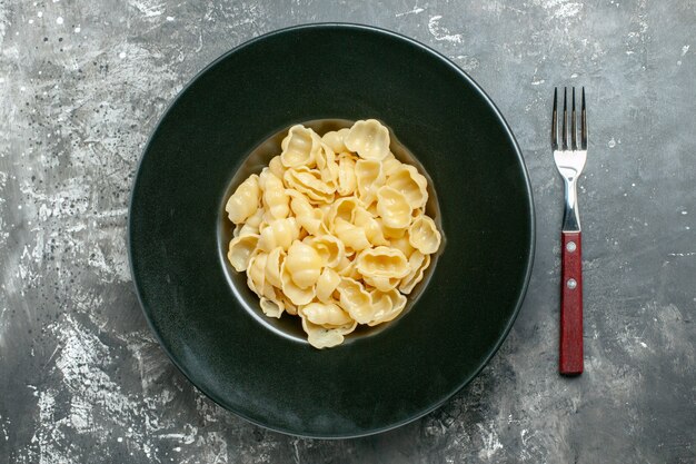 Overzichtsweergave van heerlijke conchiglie op een zwarte plaat en mes op grijze achtergrond