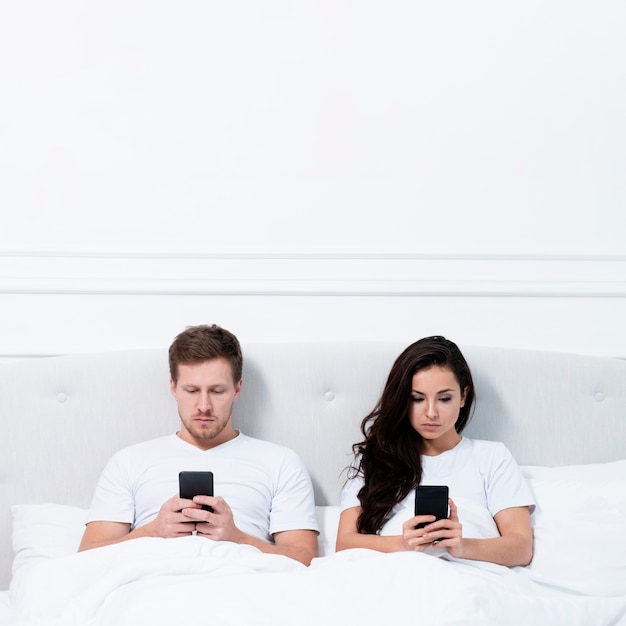 Paar dat op hun telefoons in bed blijft