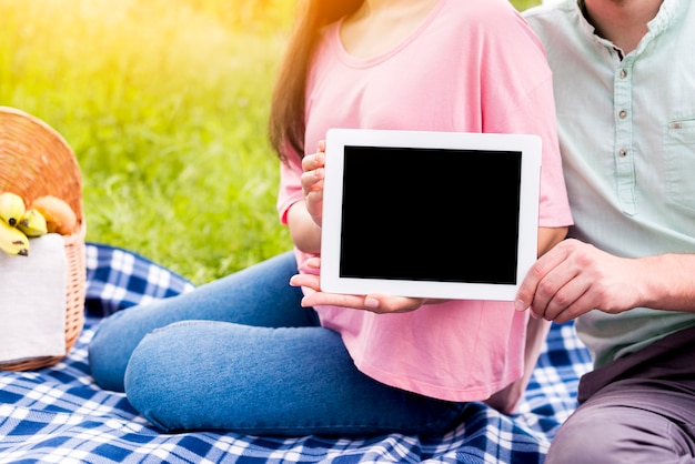 Paar dat tablet in handen op weide toont